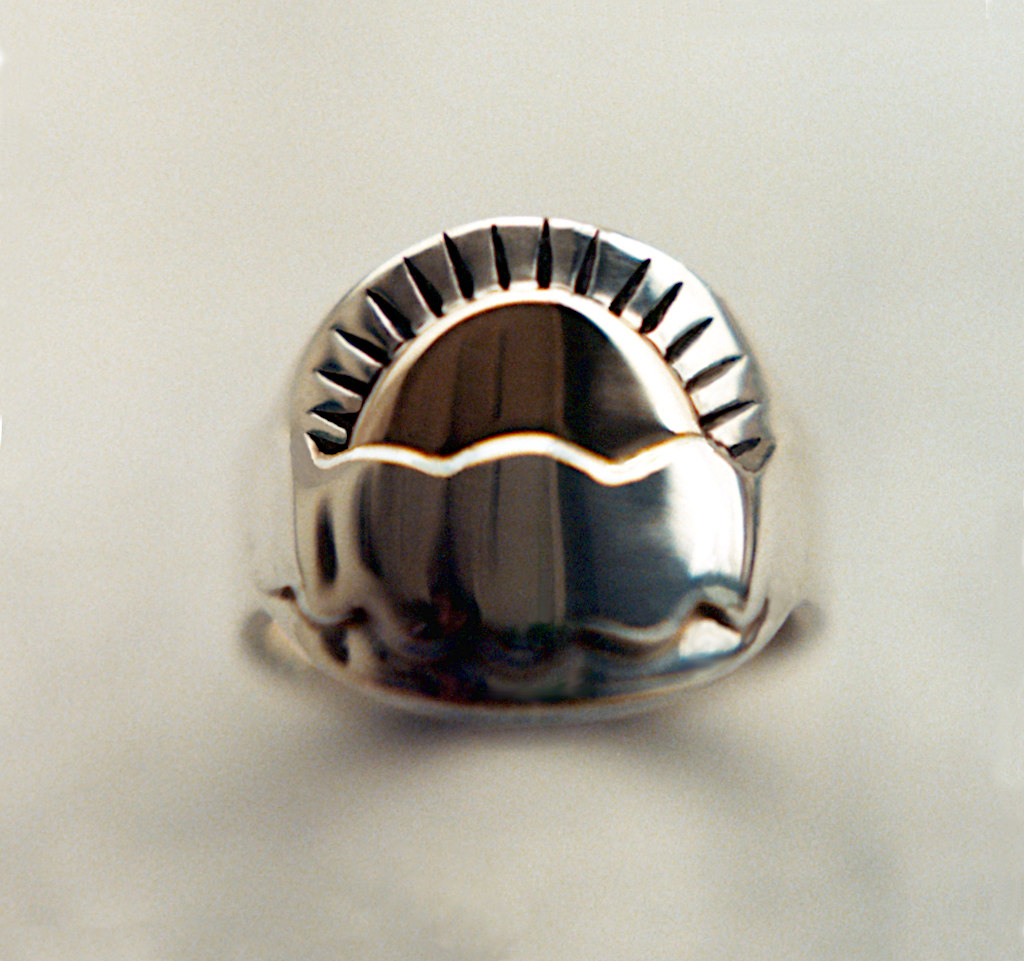 Picture of a ring that shows the sun rising from behind a cloud.