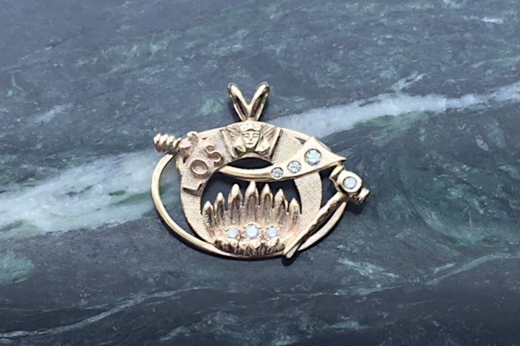 This is a picture of a 14 karat gold and diamond Past High Priestess pendant. It is sitting on a polished Vermont Serpentine slab.