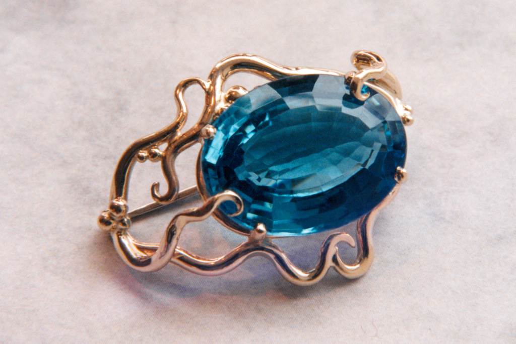 Picture of a14KY gold blue topaz pin. Stone is surrounded by gold vines.